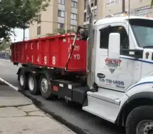 Red dumpster truck parked on a city street near buildings.