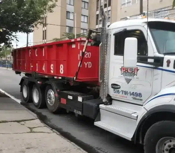 Red dumpster truck parked on a city street near buildings.